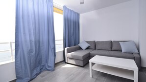 Un salon moderne avec un canapé d’angle gris, une table basse blanche et des rideaux bleus.