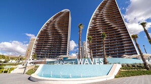 Un hôtel moderne à la façade incurvée, doté d’un espace piscine et dont l’enseigne, « Sunset Waves », est bien visible.