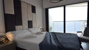 Et moderne hotelværelse med en stor seng, et sengebord, en stol og udsigt over byen gennem store vinduer.