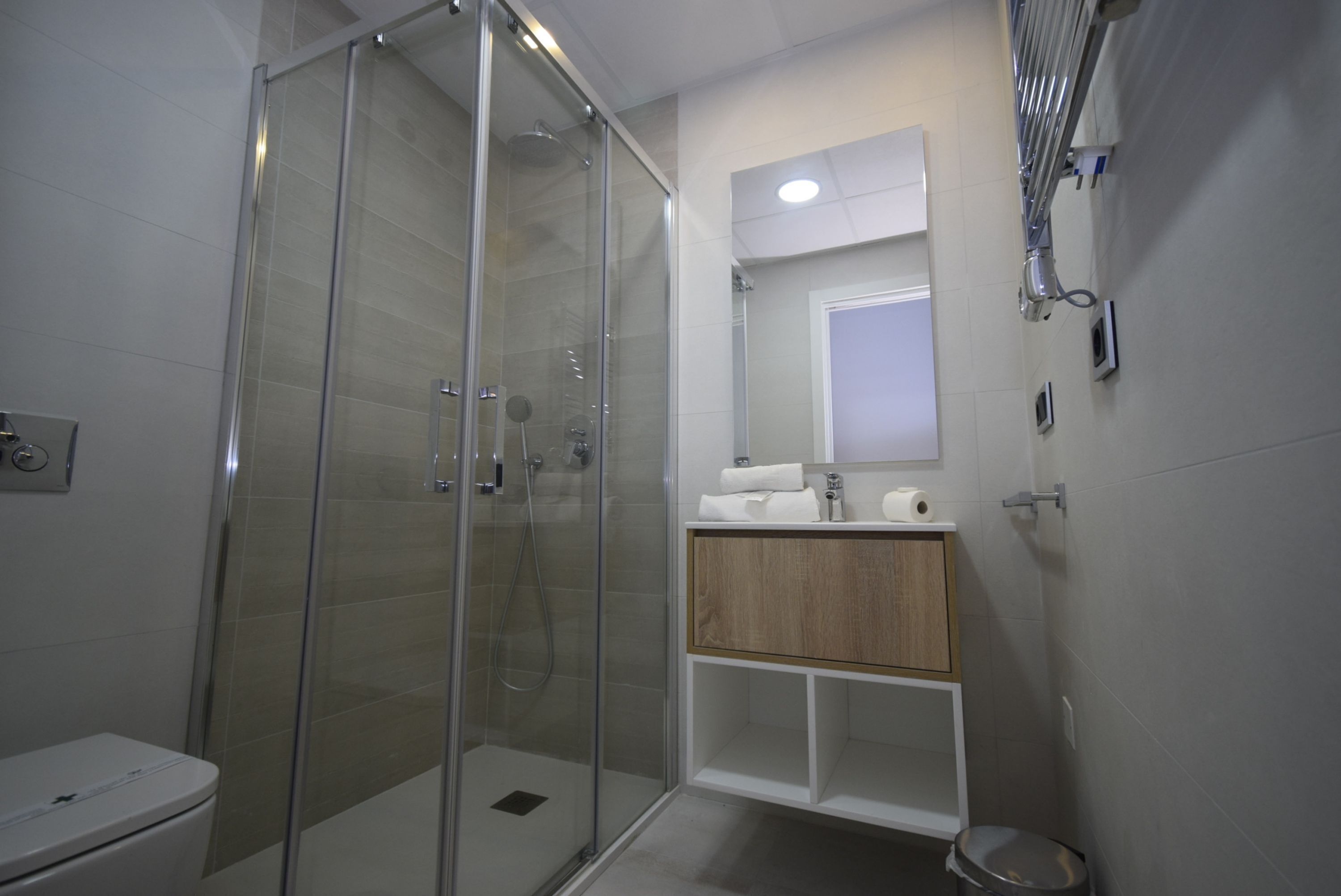 A modern bathroom with a glass-enclosed shower, a wooden vanity, and a white sink.