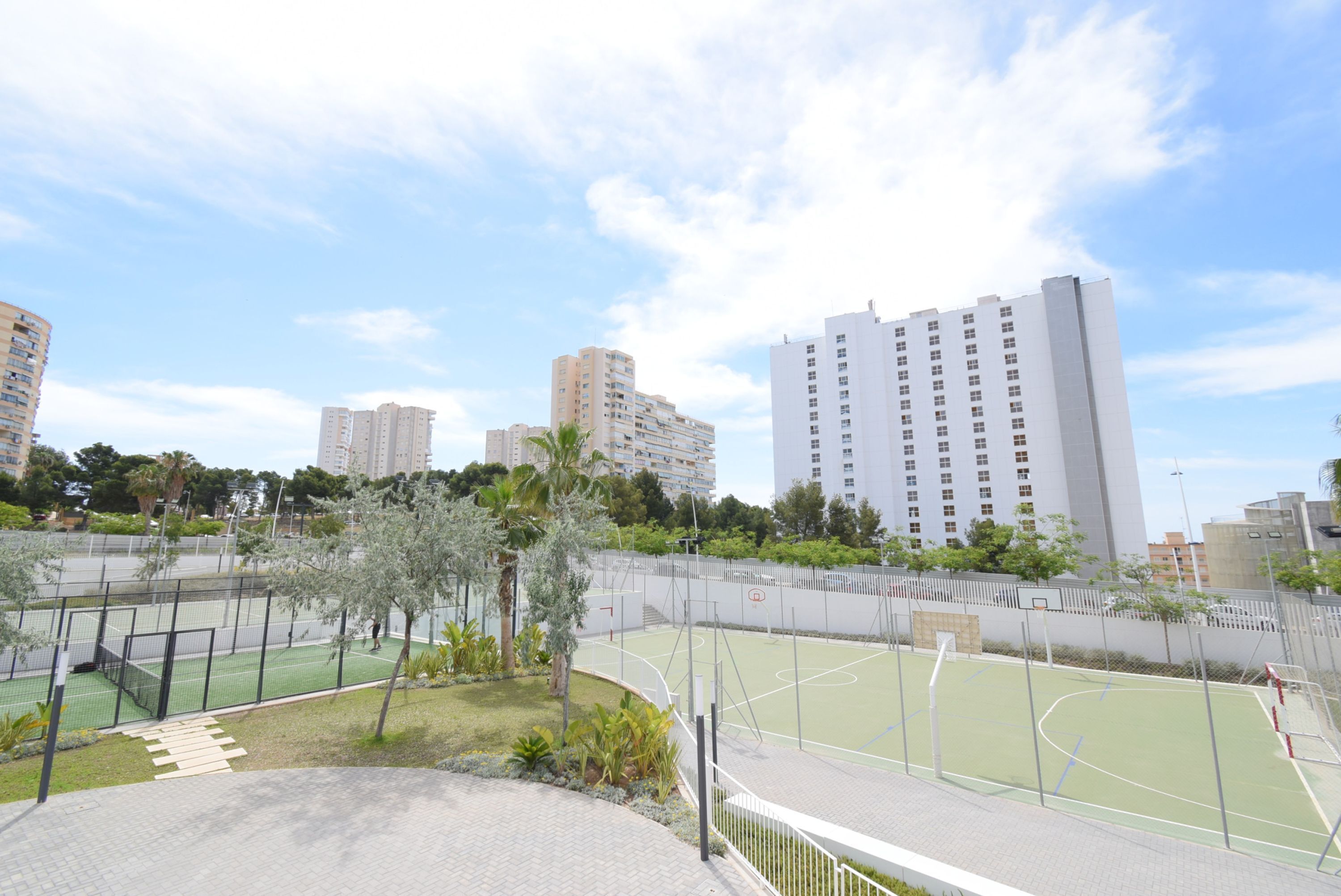 Una cancha de baloncesto rodeada por una valla, con vistas a edificios altos al fondo.