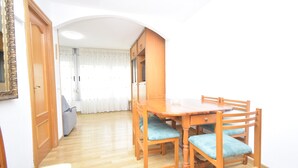 Una habitación con una mesa de comedor de madera, cuatro sillas con cojines azules, un sofá y un armario.