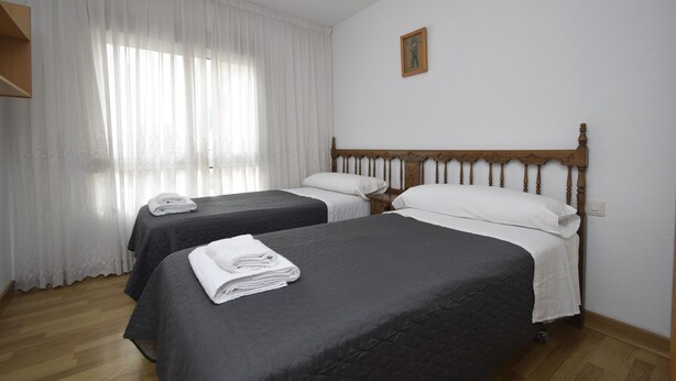 Habitación de hotel con dos camas, cabecero de madera, un cuadro en la pared y una ventana con cortinas traslúcidas.