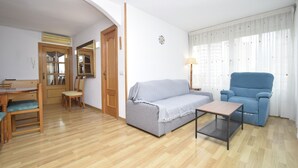 Una sala de estar con un sofá, un sillón azul, una mesita y un comedor de madera.