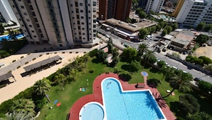Una piscina grande con cubierta roja, rodeada de palmeras y un césped.