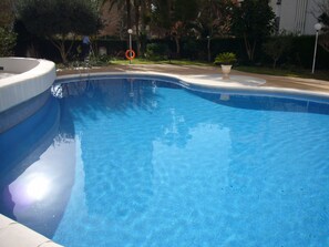 A swimming pool with a curved edge, surrounded by a paved area and greenery. - Parque Europa 5B1 in Benidorm (Benidorm)