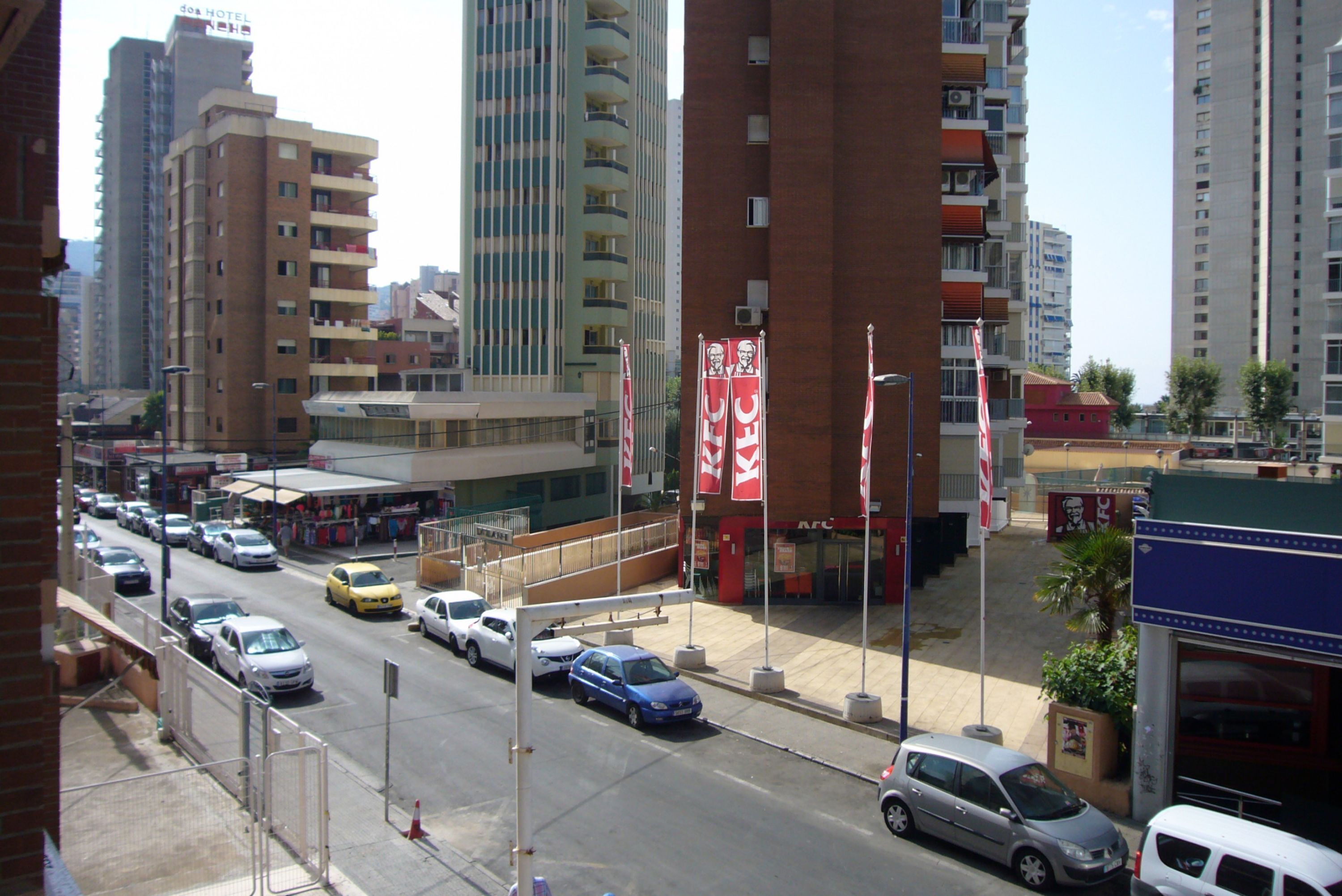 Eine belebte Stadtstraße mit mehreren Autos, einem KFC-Restaurant und hohen Gebäuden.
