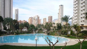 A swimming pool surrounded by greenery and tall buildings in the background. - Gemelos 22 13c3 in Benidorm (Benidorm)
