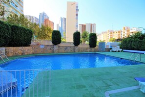 A swimming pool with a stone wall and greenery, surrounded by high-rise buildings. - Cadiz 4B in Benidorm (Benidorm)
