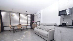 A modern living room with a sofa, dining table, chairs, and a kitchen area with a microwave. - Coblanca 29 - T2 16-5 (Benidorm)