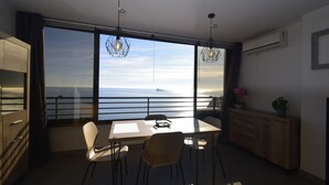 Eine moderne Küche mit einem großen Fenster mit Meerblick, einem Esstisch mit Stühlen und einem Holzschrank.