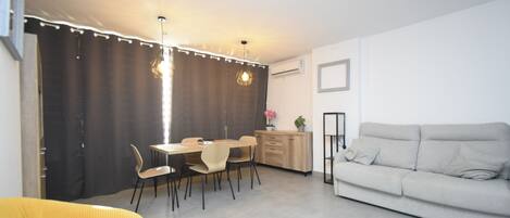 Een moderne woonkamer met een bank, een eettafel, stoelen en een hanglamp.