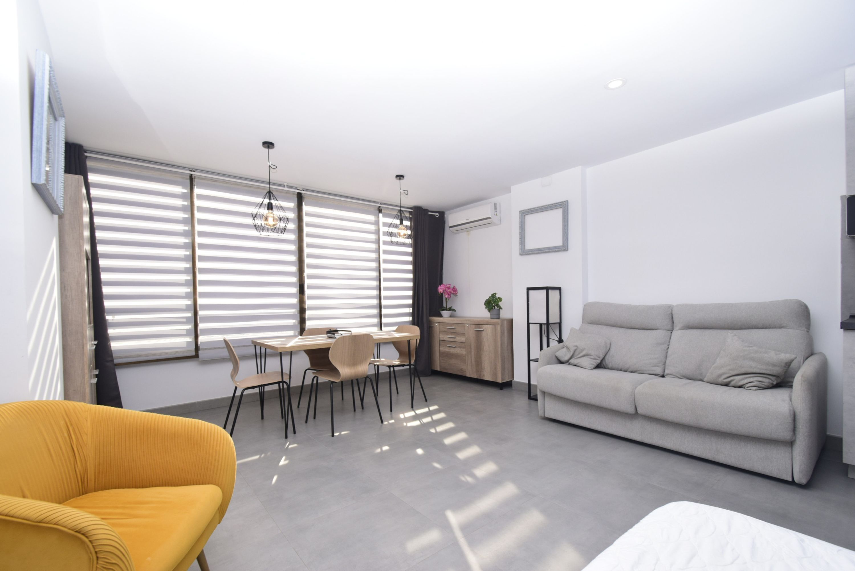Una sala de estar moderna con un sofá, una mesa de comedor, sillas y un sillón amarillo.