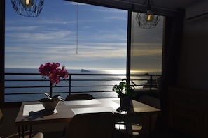 A dining area with a view of the sea and a sunset.