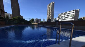 Ein Schwimmbecken mit einer gefliesten Kante, Metallhandläufen und Blick auf umliegende Hochhäuser.