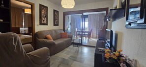 A living room with a sofa, armchair, TV, and a small table with flowers. There is a dining area visible through a glass door. - Cachirulo 6D in Benidorm (Benidorm)