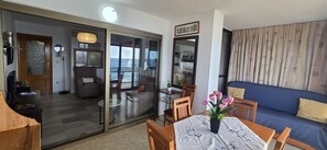 A living room with a blue sofa, a dining table with a vase of flowers, and a view of the sea through a sliding glass door. - Cachirulo 6D in Benidorm (Benidorm)