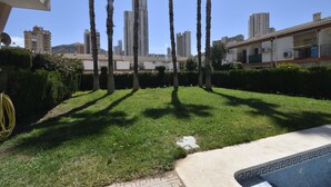 A courtyard with a swimming pool, palm trees, and a cityscape in the background. - Mariscal 6 8B in Benidorm (Benidorm)