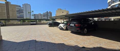 Un'area di parcheggio con diverse auto, una struttura coperta e edifici sullo sfondo.