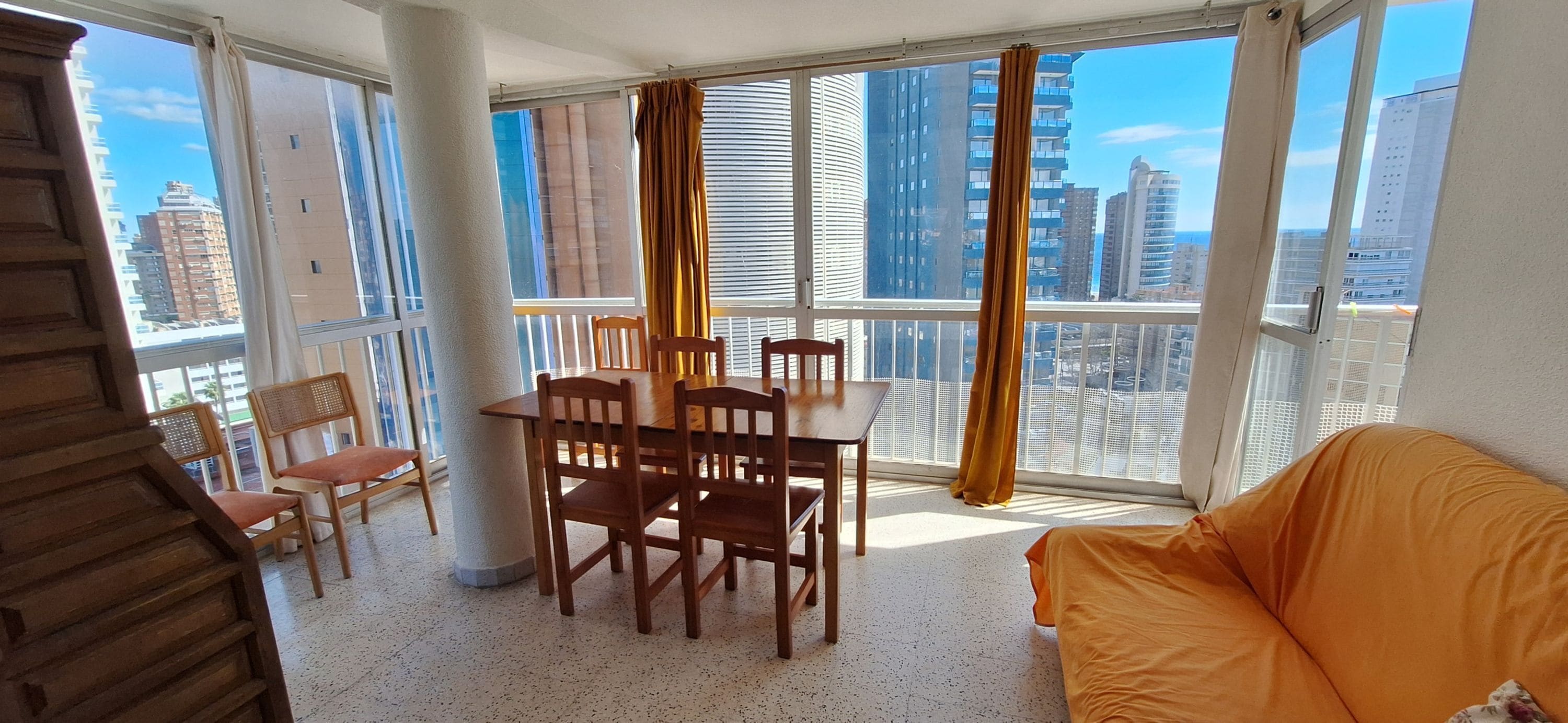 A balcony with a dining table and chairs, a sofa, and a view of tall buildings.