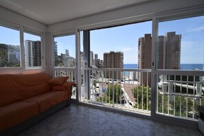 Ein Zimmer mit großem Balkon, einer Couch und Blick auf Stadt und Meer.