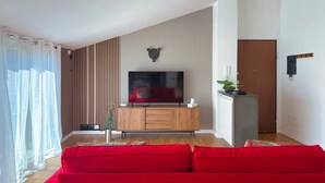 A modern living room with a large flat-screen TV, a wooden cabinet, and a red sofa. - Il Terrazzo di Betta With Garage 15 min to Duomo (Milan)