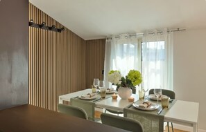 Un coin repas avec une table blanche dressée pour deux personnes, un vase rempli de fleurs et un mur recouvert de lambris en bois.
