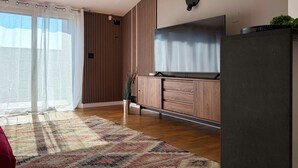 A modern living room with a large flat-screen TV, wooden panel walls, a sliding glass door, and a patterned rug. - Il Terrazzo di Betta With Garage 15 min to Duomo (Milan)