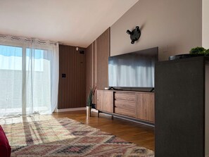 Un salon moderne doté d’un grand téléviseur à écran plat, de murs recouverts de panneaux en bois, d’une porte-fenêtre coulissante et d’un tapis à motifs.