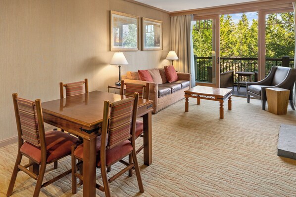 Une chambre d’hôtel équipée d’une table à manger, de chaises, d’un canapé et d’un balcon offrant une vue sur les arbres.