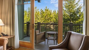 A hotel room with a sliding glass door leading to an outdoor balcony with a view of trees.