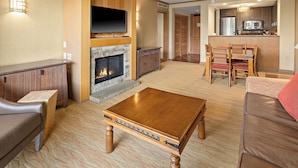 A living room with a fireplace, wooden furniture, and a kitchen area.