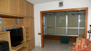 Un salon avec des meubles en bois, un téléviseur, un canapé et une fenêtre équipée de stores.