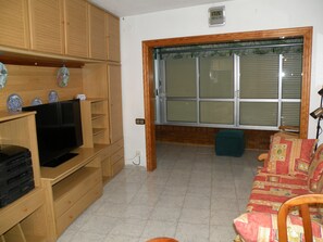 A living room with wooden cabinets, a television, a sofa, and a window with blinds. - Acacias 4 7B in Benidorm (Benidorm)