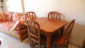 Un coin repas avec une table en bois et quatre chaises, un canapé agrémenté de coussins colorés et un sol carrelé.