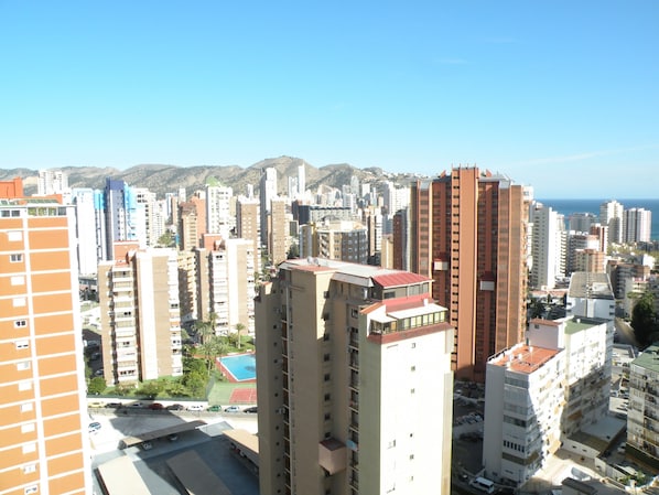 A high-rise building with multiple floors, a parking area in front, and a view of the cityscape and mountains in the background. - Acacias 4 7B in Benidorm (Benidorm)