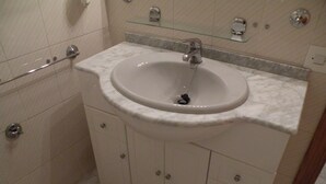 Une salle de bain avec un lavabo blanc, un plan de toilette en marbre et une étagère en verre au-dessus du lavabo.