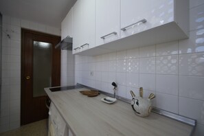 Una cocina con armarios blancos, una puerta de madera y una encimera con un escurreplatos, un plato pequeño y un jarrón decorativo.