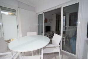A modern interior with a white dining table and chairs, a television, and a sliding glass door leading to a balcony. - Caballos 8E Estudio (Benidorm)