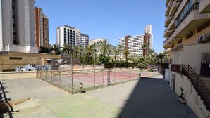 A tennis court surrounded by buildings, with a clear sky. - Acuarium 3 2F Estudio (Benidorm)