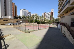 Ein Tennisplatz, umgeben von Gebäuden, mit blauem Himmel.