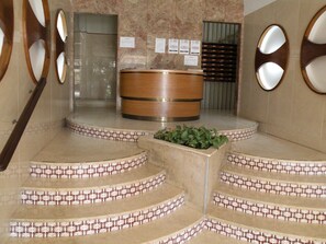 A reception area with a wooden reception desk, a plant in a planter, and a set of stairs with patterned tiles. - Ducado 8D in Benidorm (Benidorm)