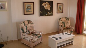 Ein Wohnzimmer mit zwei Sesseln, einem Couchtisch und drei gerahmten Kunstwerken an der Wand.