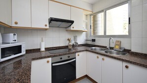 A modern kitchen with white cabinets, granite countertops, a built-in oven, a microwave, and a window providing natural light. - Marina Baixa 3D in Cala de Finestrat (Finestrat)
