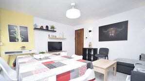 A modern living room with a dining area, a flat-screen TV, a wooden door, and a bull-themed artwork on the wall. - Marina Baixa 3D in Cala de Finestrat (Finestrat)