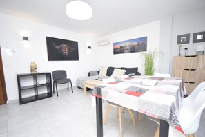 A modern living room with a dining table, sofa, and a large window. - Marina Baixa 3D in Cala de Finestrat (Finestrat)