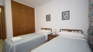 Een hotelkamer met twee eenpersoonsbedden, een houten kledingkast en twee ingelijste foto’s aan de muur.