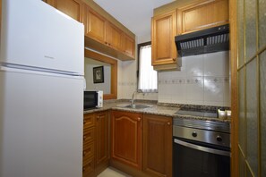 Eine Küche mit Holzschränken, einem Edelstahlkühlschrank, einer Mikrowelle, einem Spülbecken und einem Backofen.
