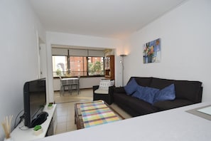 A living room with a black sofa, a TV, a coffee table, and a dining area with a table and chairs. - Gemelos 5 4C in Benidorm (Benidorm)