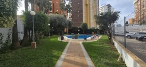 A swimming pool surrounded by greenery, with a pathway leading to it. Tall buildings are visible in the background. - Gemelos 5 4C in Benidorm (Benidorm)